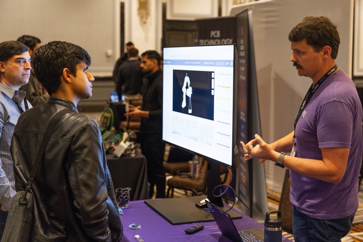 Two attendees at a sponsor stand on the Kinetic 2026 floor, watching a demo on a monitor.