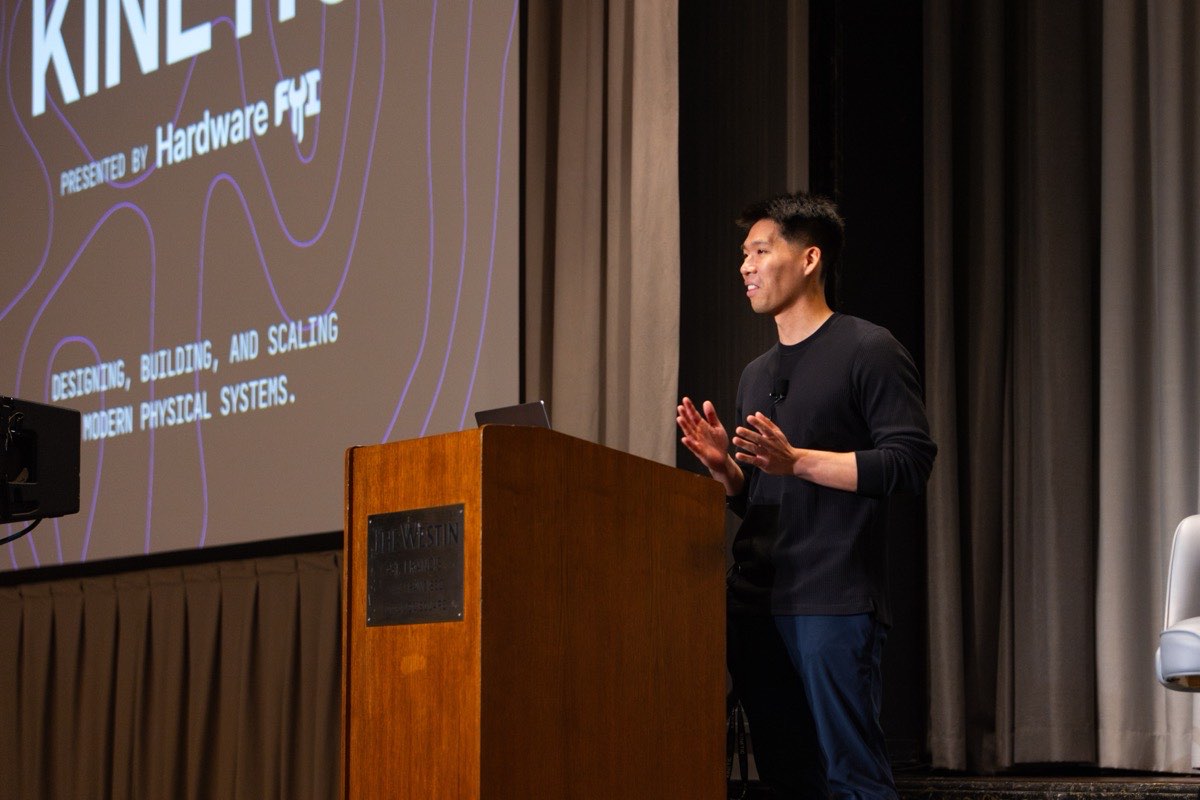 A speaker on stage at Kinetic 2026, the Kinetic title slide on the screen behind him.