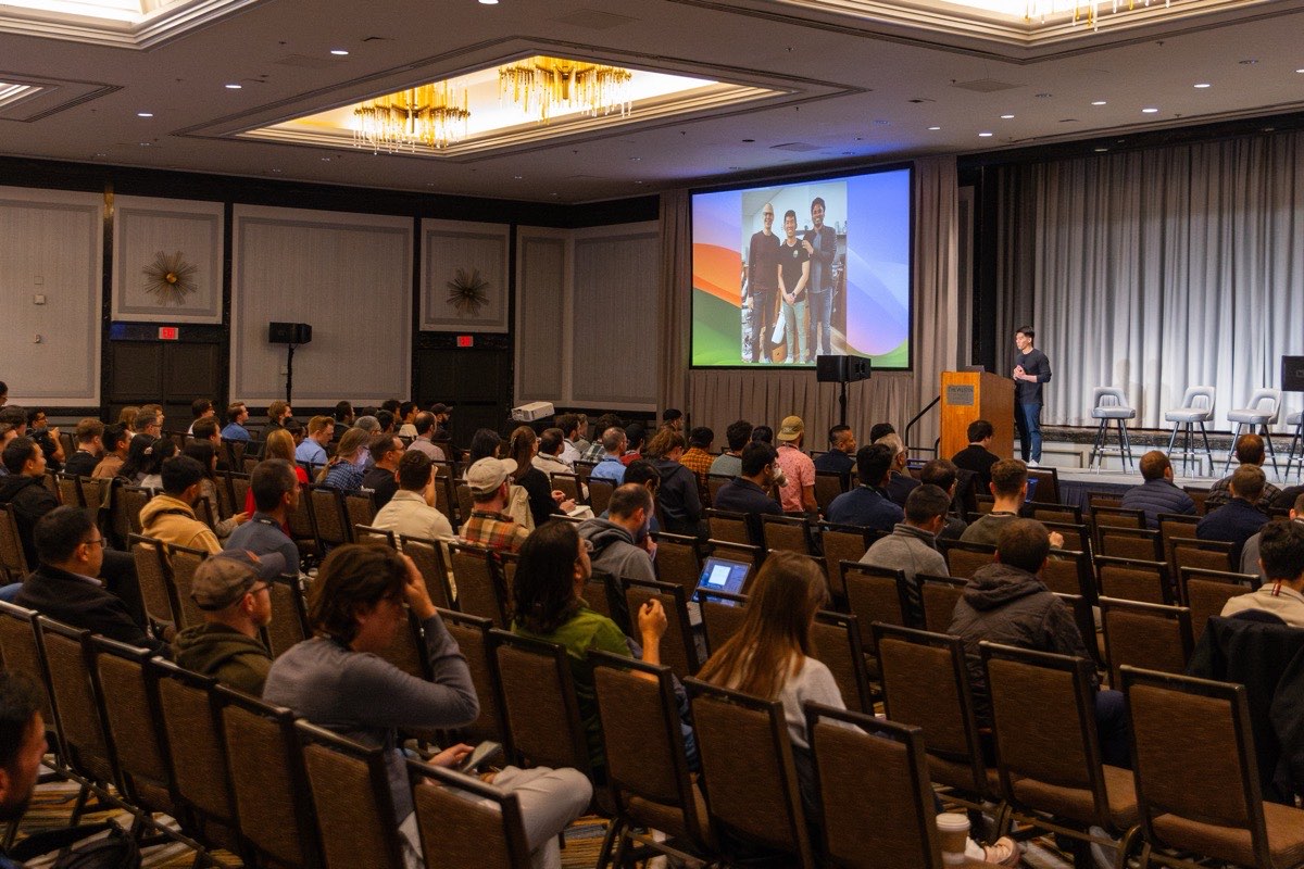 The main room at Kinetic 2026, every seat taken, a speaker at the podium.